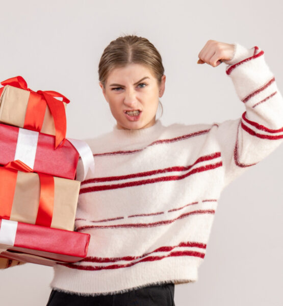 Eine Frau hält in einer Hand mehrere Geschenke und spannt den Bizeps des anderen Arms an.