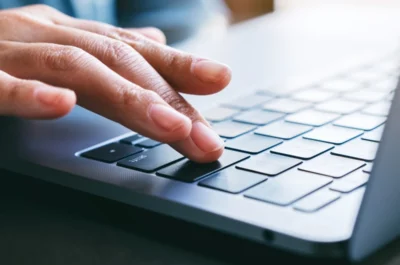 Hand bestätigt eine Eingabe auf der Tastatur eines Laptops per Enter-Taste.