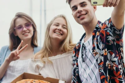 3 junge Erwachsene machen ein Selfie zusammen mit einer Pizza im Karton.