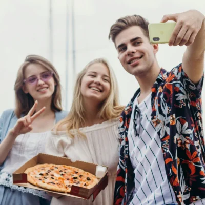 3 junge Erwachsene machen ein Selfie zusammen mit einer Pizza im Karton.