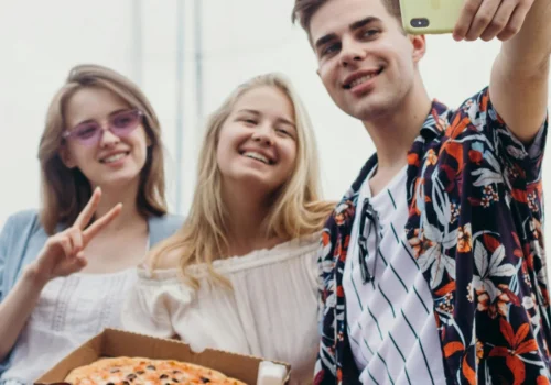 3 junge Erwachsene machen ein Selfie zusammen mit einer Pizza im Karton.