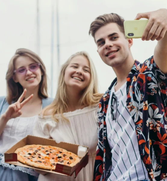 3 junge Erwachsene machen ein Selfie zusammen mit einer Pizza im Karton.