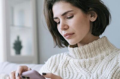 Frau auf der Couch schaut mit einem ernsten Gesichtsausdruck auf ihr Handy