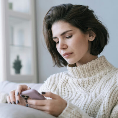 Frau auf der Couch schaut mit einem ernsten Gesichtsausdruck auf ihr Handy