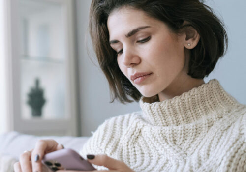 Frau auf der Couch schaut mit einem ernsten Gesichtsausdruck auf ihr Handy