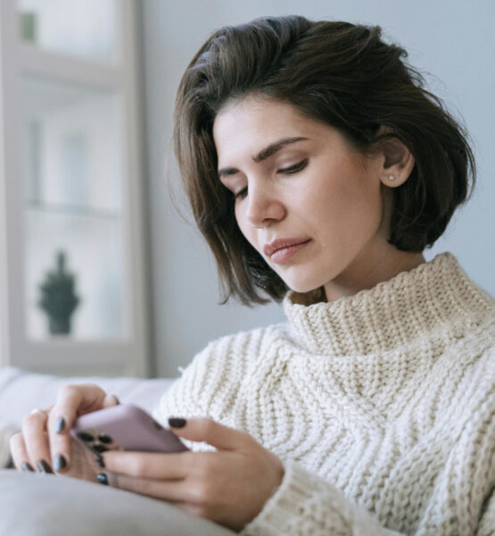 Frau auf der Couch schaut mit einem ernsten Gesichtsausdruck auf ihr Handy