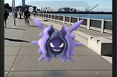 Ein Screenshot aus Pokémon GO zeigt ein lilafarbenes Pokémon (Cloyster), das scheinbar auf einem Gehweg an einer Uferpromenade schwebt. Im Hintergrund sind ein Geländer, Wasser, ein Fahrradfahrer und ein Turm zu sehen, während die reale Umgebung mit der Augmented-Reality-Darstellung kombiniert wird.