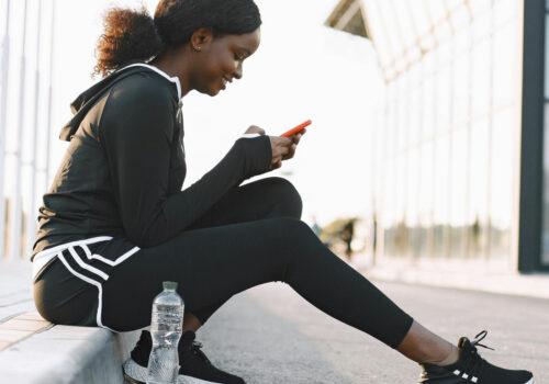 Frau im Trainingsanzug sitzt auf der Bordsteinkante und bedient ihr Smartphone
