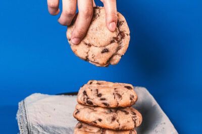 Eine Hand hebt vor blauem Hintergrund einen Schokokeks von einem Stapel hoch