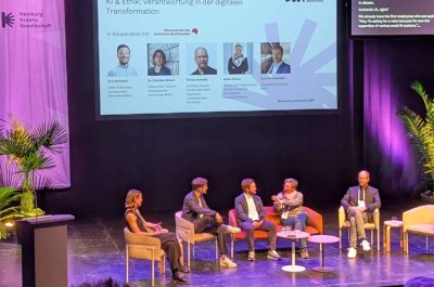 Fünf Personen unterhalten sich bei einer Panel-Diskussion auf einer Bühne, im Hintergrund ist das Logo des German Creative Economy Summit zu sehen