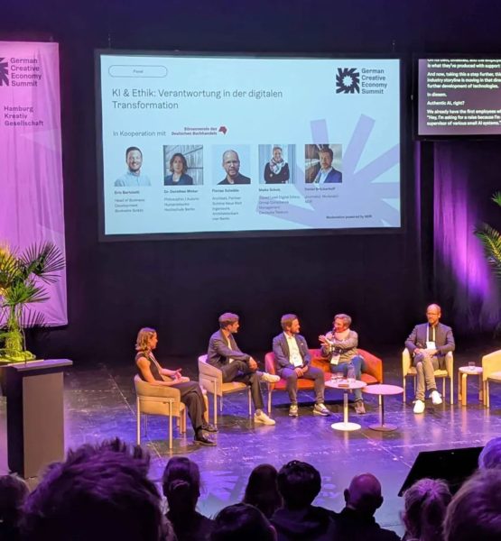 Fünf Personen unterhalten sich bei einer Panel-Diskussion auf einer Bühne, im Hintergrund ist das Logo des German Creative Economy Summit zu sehen