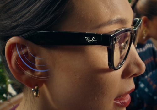 Frau trägt die Meta x RayBan Brille, an ihrem Ohr werden durch blaue Signalstreifen der Lautsprechereffekt der Brille signalisiert