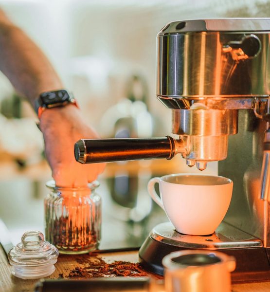 Hand bedient einen Siebträger an einer Edelstahl-Espressomaschine, davor eine weiße Tasse