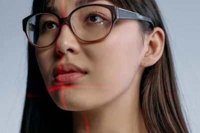Eine Frau trägt eine Brille und schaut an der Kamera vorbei, während sich rote Laserstrahlen sich in ihrem Gesicht kreuzen