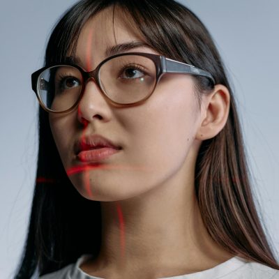 Eine Frau trägt eine Brille und schaut an der Kamera vorbei, während sich rote Laserstrahlen sich in ihrem Gesicht kreuzen