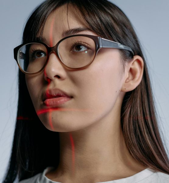 Eine Frau trägt eine Brille und schaut an der Kamera vorbei, während sich rote Laserstrahlen sich in ihrem Gesicht kreuzen