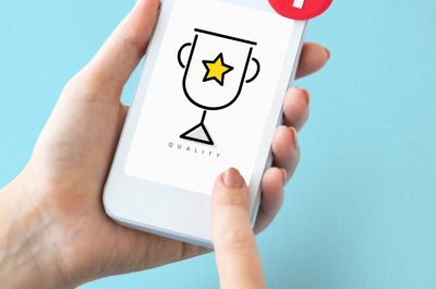 Smartphone in der Hand auf dessen Bildschirm ein Siegerpokal angezeigt wird.