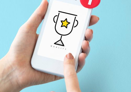 Smartphone in der Hand auf dessen Bildschirm ein Siegerpokal angezeigt wird.