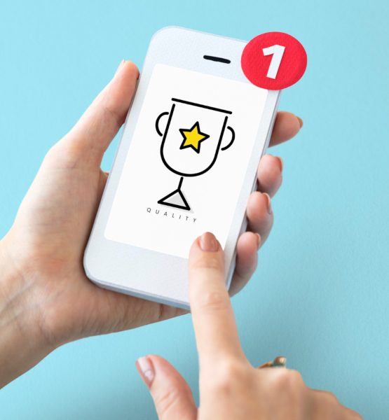 Smartphone in der Hand auf dessen Bildschirm ein Siegerpokal angezeigt wird.