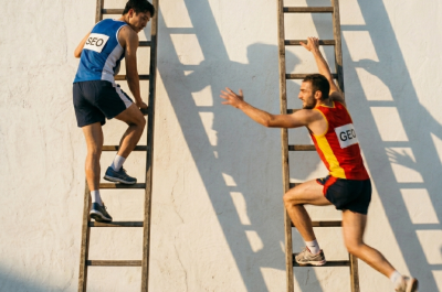 Notiert. Two athletes mid-race, both climbing separate tall ladders leaning against a white wall. The left climber, labeled "SEO" on their jersey, is near the top but visibly slowing down. The right climber, labeled "GEO" on their jersey, is several rungs below but lunging upward with visible effort and speed — one arm outstretched reaching for the next rung. Dynamic action photography style, motion blur on the GEO climber, dramatic side lighting, strong shadows. Realistic, energetic, cinematic. Square format 1:1 aspect ratio, output as PNG, file size under 1MB.