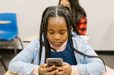 Ein junges Mädchen sitzt an einem Tisch in ihrem Klassenzimmer und schaut auf ihr Smartphone.