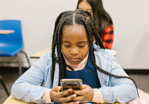 Ein junges Mädchen sitzt an einem Tisch in ihrem Klassenzimmer und schaut auf ihr Smartphone.
