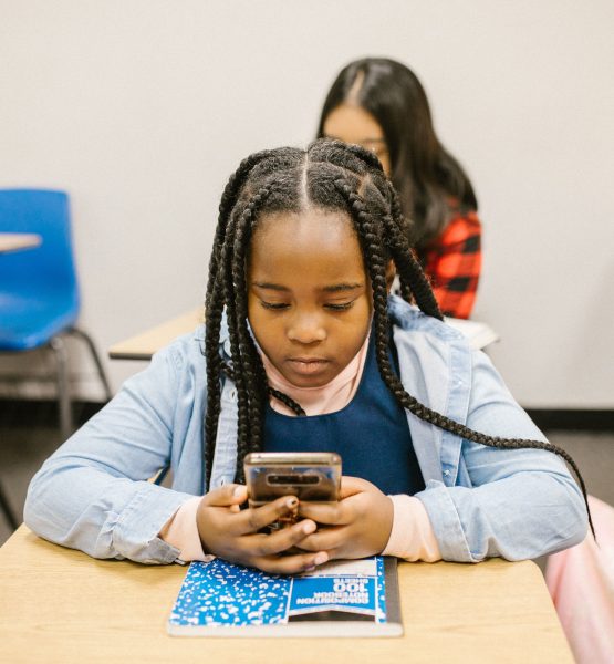 Ein junges Mädchen sitzt an einem Tisch in ihrem Klassenzimmer und schaut auf ihr Smartphone.