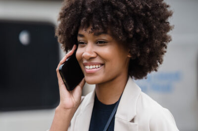 Eine Frau hält ihr Smartphone in der Hand und lächelt während sie damit telefoniert