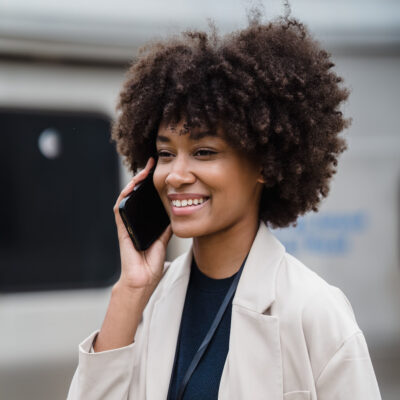 Eine Frau hält ihr Smartphone in der Hand und lächelt während sie damit telefoniert