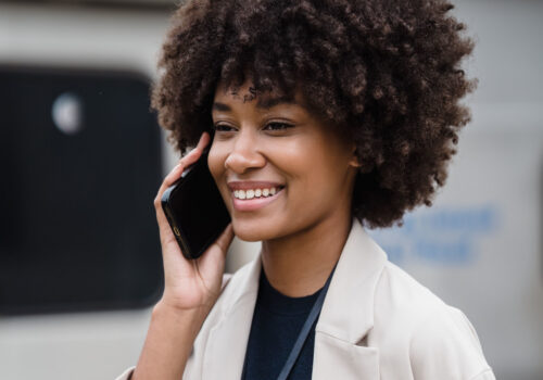 Eine Frau hält ihr Smartphone in der Hand und lächelt während sie damit telefoniert