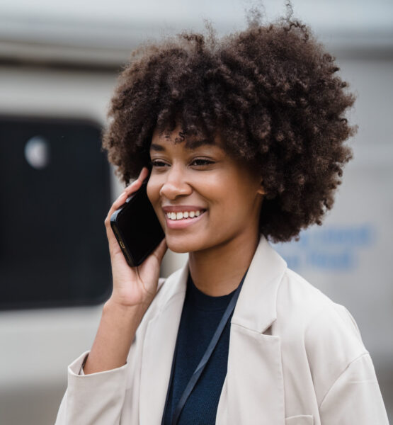 Eine Frau hält ihr Smartphone in der Hand und lächelt während sie damit telefoniert