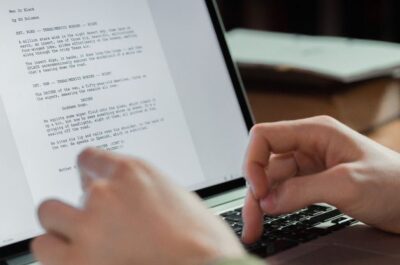 Hände tippen auf einem Laptop ein Manuskript.