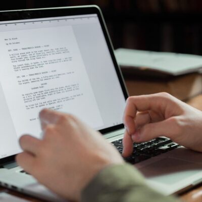 Hände tippen auf einem Laptop ein Manuskript.