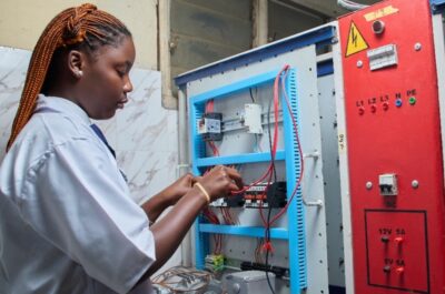 Young female technician repairing electrical control panel in industrial setting.