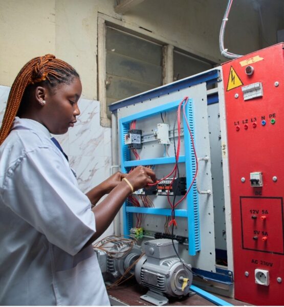 Young female technician repairing electrical control panel in industrial setting.